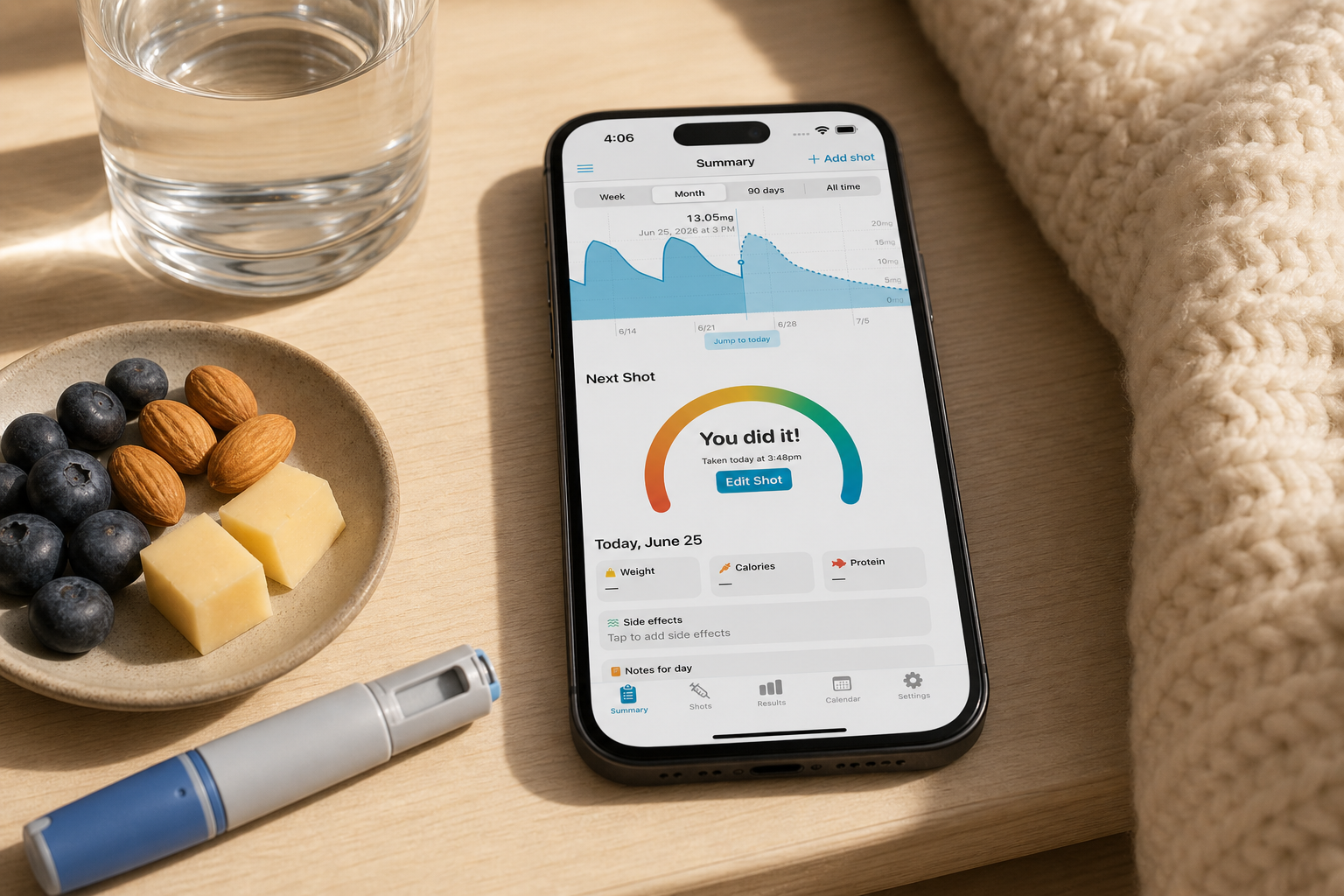 Shotsy app on a phone beside water, a protein snack, blanket, and GLP-1 injection pen