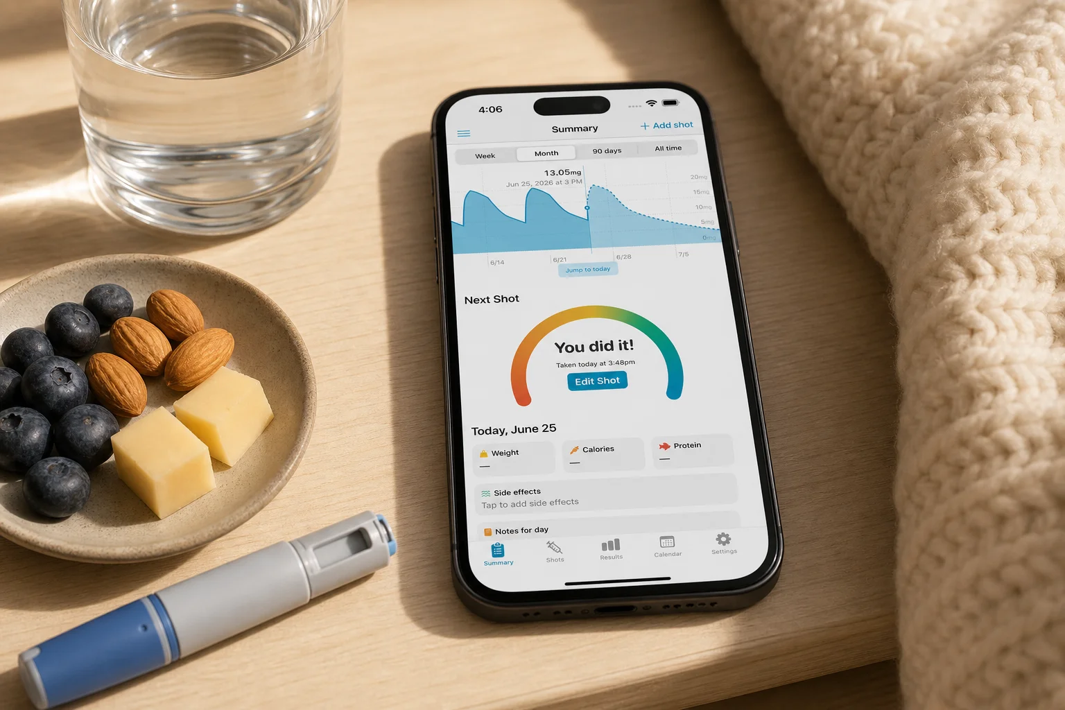 Shotsy app on a phone beside water, a protein snack, blanket, and GLP-1 injection pen