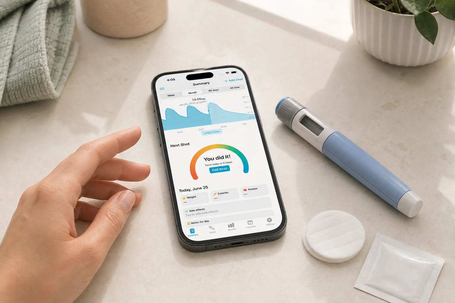 Shotsy app on a phone beside a GLP-1 injection pen, alcohol swab, and cotton pad